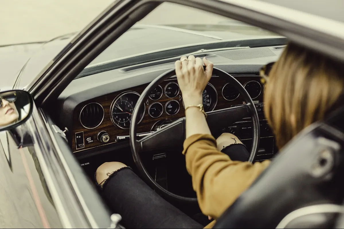 Person driving a classic car seen through the open driver door