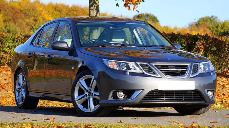 Dark grey Saab 9-3 sedan parked on a road lined with autumn trees