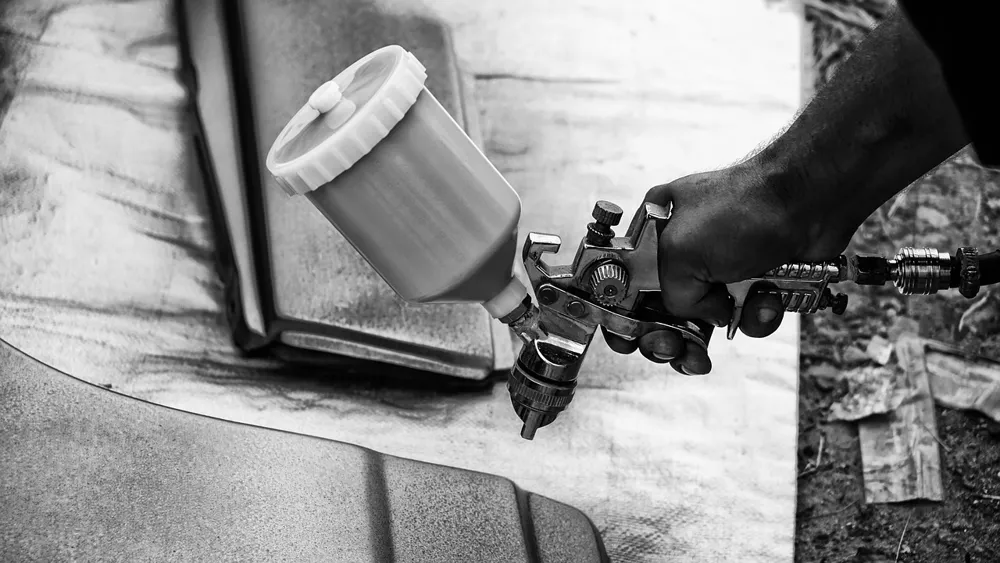 Hand holding a gravity-feed spray gun over a car panel