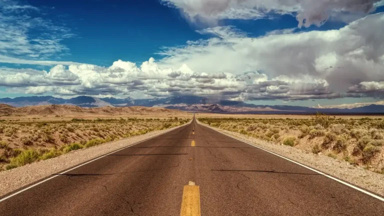 Empty two-lane highway running toward distant mountains under a cloudy sky
