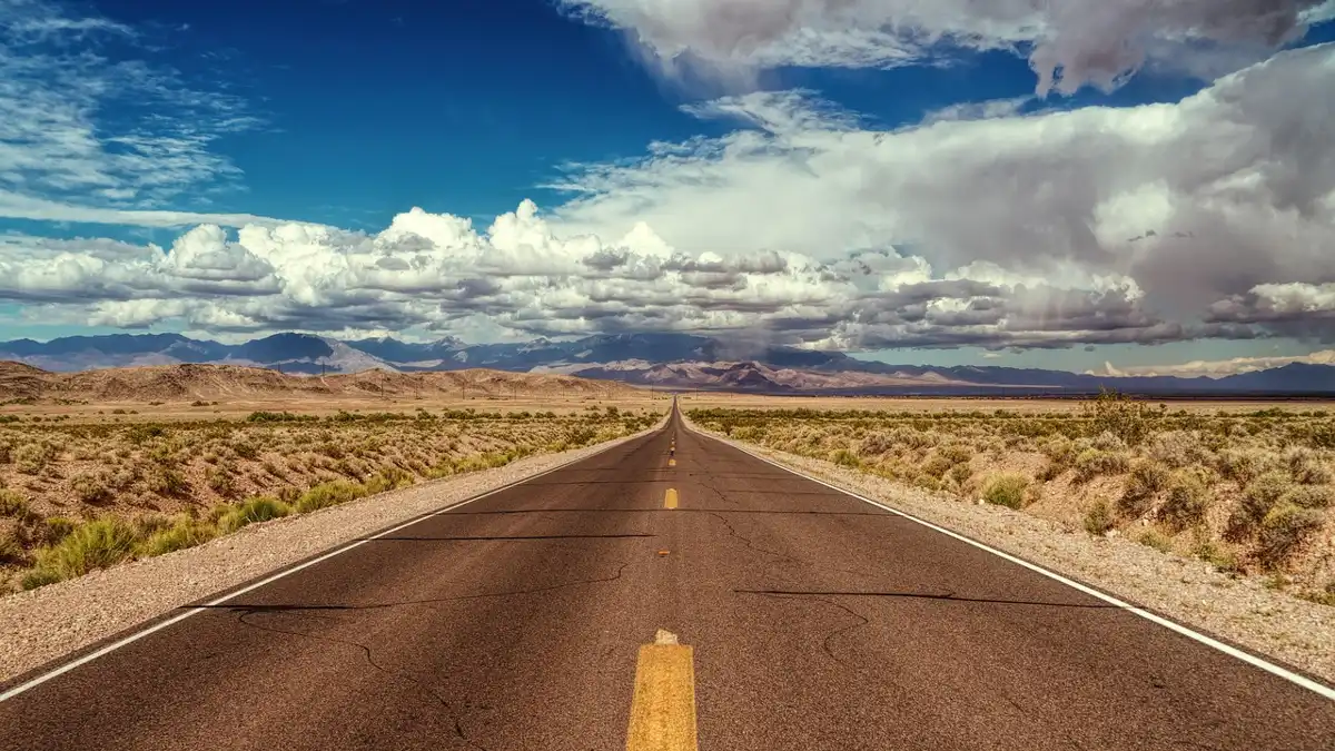 Empty two-lane highway running toward distant mountains under a cloudy sky
