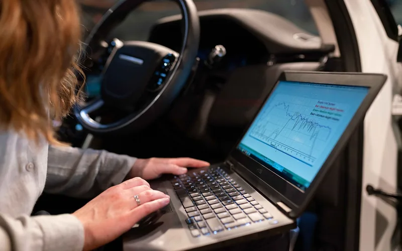 Person using a laptop in the driver seat of a car for vehicle diagnostics Person using a laptop in the driver seat of a car for vehicle diagnostics