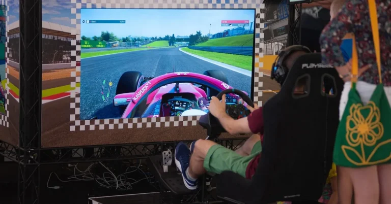 Person racing on a car simulator cockpit rig with steering wheel and pedals at a gaming expo