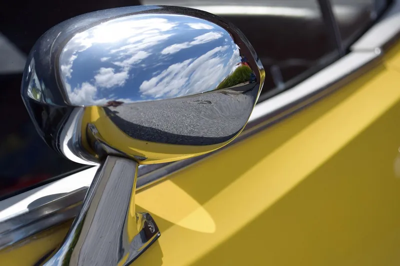 Chrome side mirror on a yellow car door reflecting clouds and sky