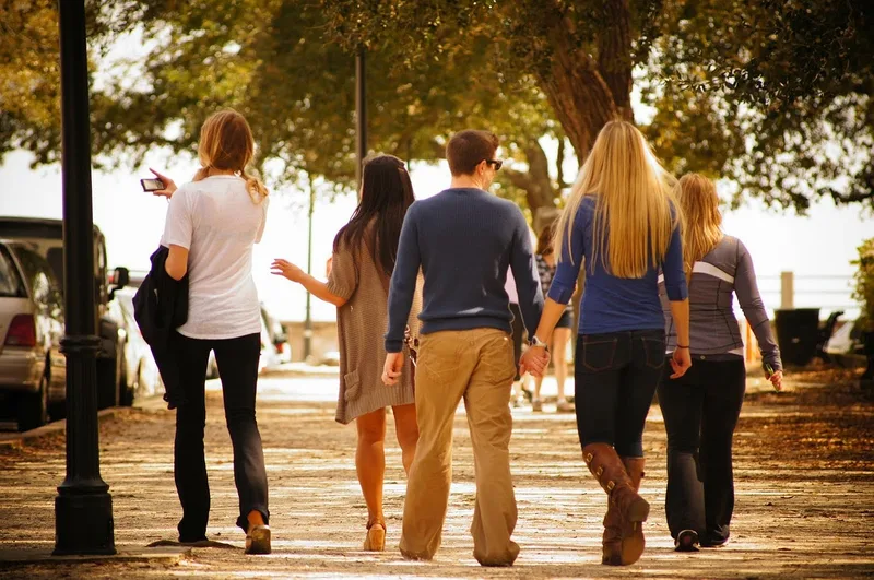 Group of five friends walking together along a tree-lined path