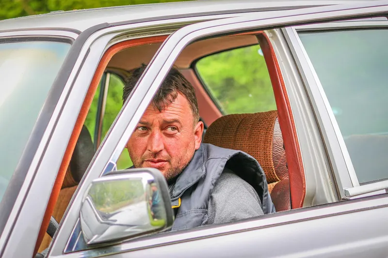 Man seated at the wheel of a car looking out of the open window beside the side mirror