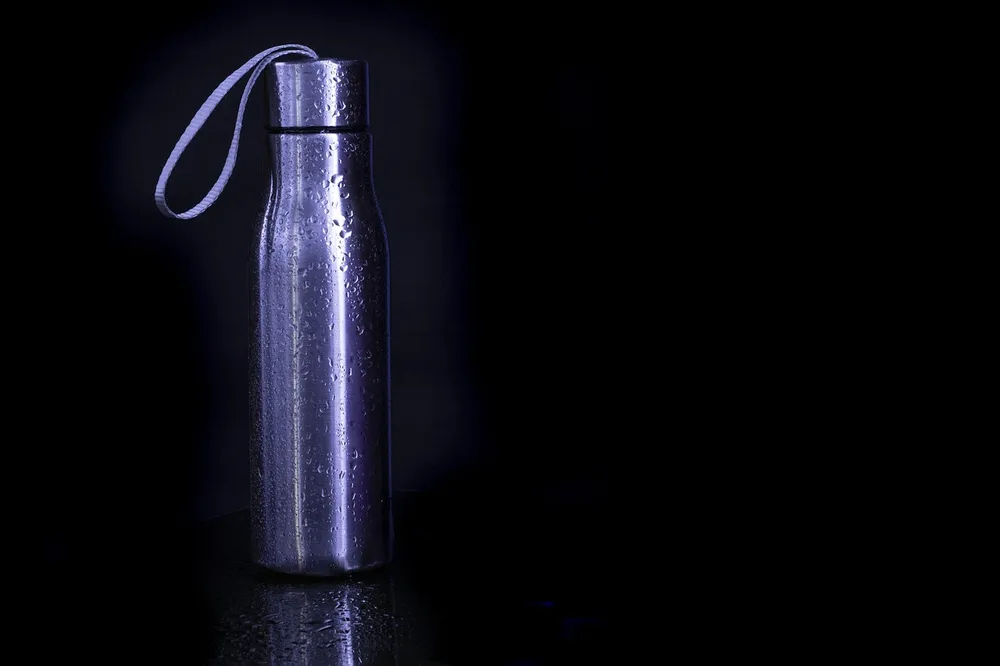 A stainless steel water bottle with a carry strap loop and water droplets on a dark background