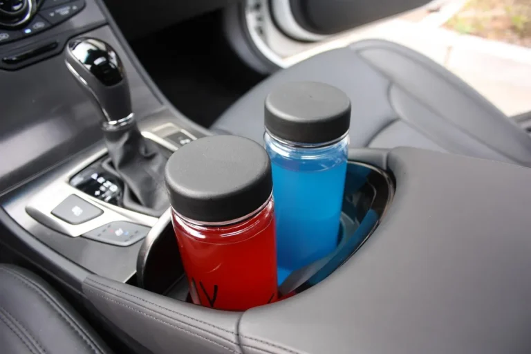 Two capped bottles, one with red drink and one with blue, standing in a car center console cup holder