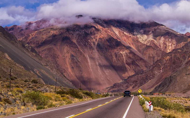 SUV driving a paved mountain highway toward a high red-rock peak SUV driving a paved mountain highway toward a high red-rock peak with a curve warning sign