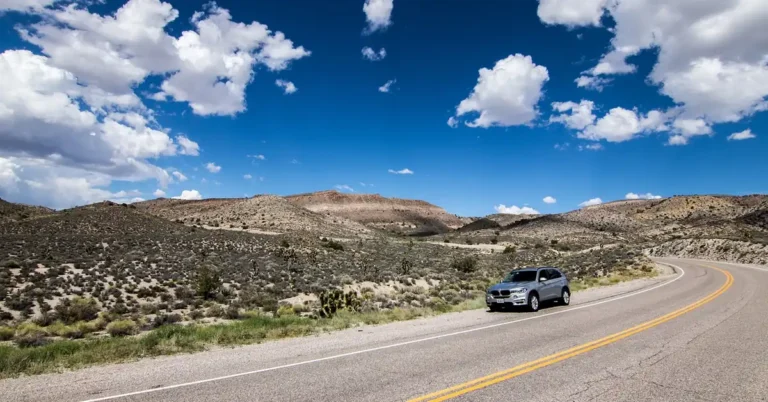 A silver SUV on a two lane road under a wide open sky