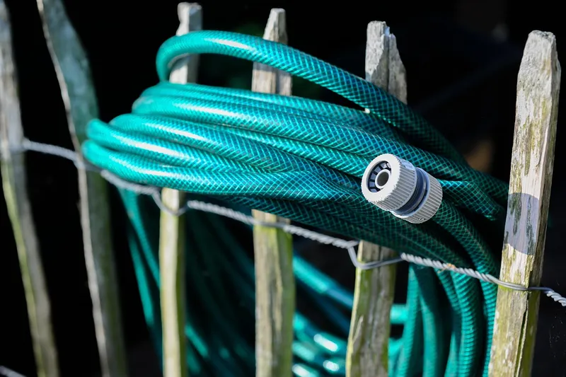 Coiled green garden hose with a grey threaded connector hung on a wooden fence