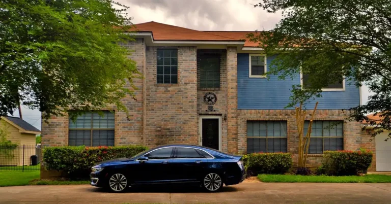 Dark sedan parked in a driveway in front of a brick house