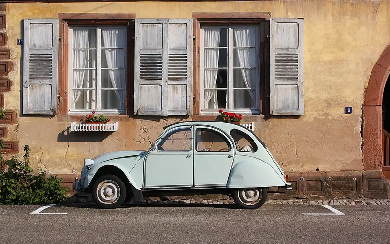 Older pale-green small car parked in front of a stone building Older pale-green small car parked in front of a stone building