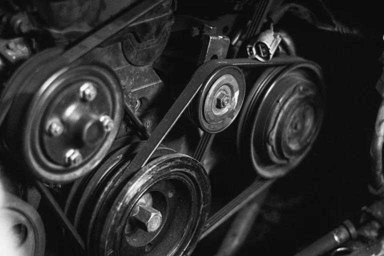 Black and white close-up of an engine drive belt running over accessory pulleys and a tensioner