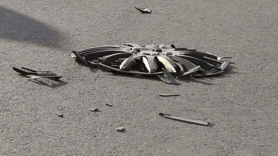 A broken plastic wheel cover and fragments lying on an asphalt road