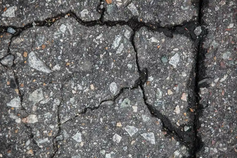 Cracked asphalt pavement with exposed stones and dark cracks