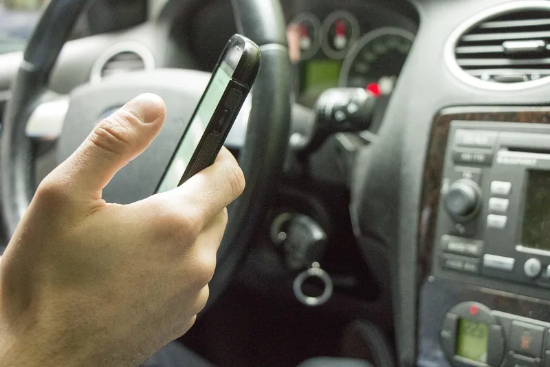 Hand holding a smartphone near the steering wheel