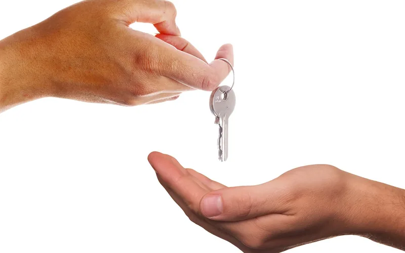 One hand passing a single metal key to another open hand