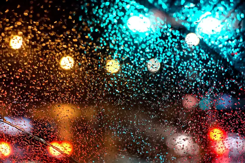 Rain drops on a windshield at night with blurred traffic lights behind them