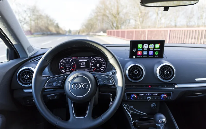Car dashboard touchscreen displaying a CarPlay-style app interface next to the steering wheel