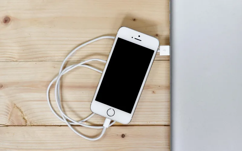 iPhone connected to a white Lightning cable lying on a wooden table