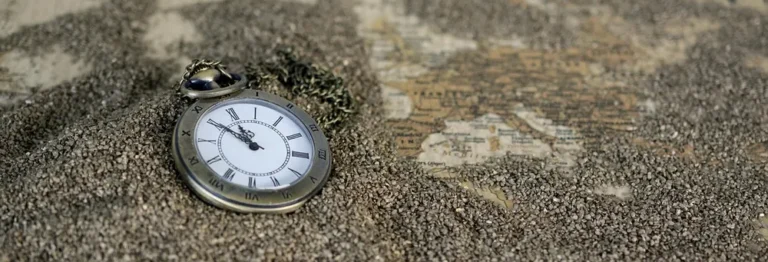 Pocket watch lying in sand on top of an old map