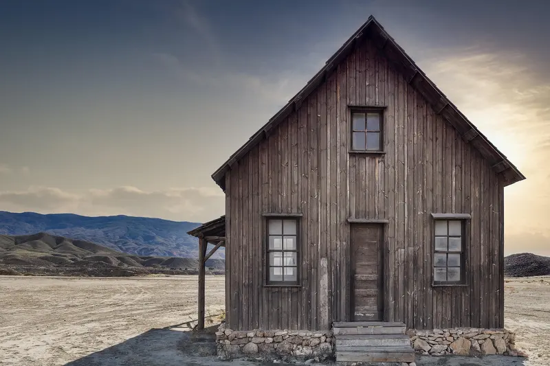 Weathered wooden house standing on dry desert ground at sunset