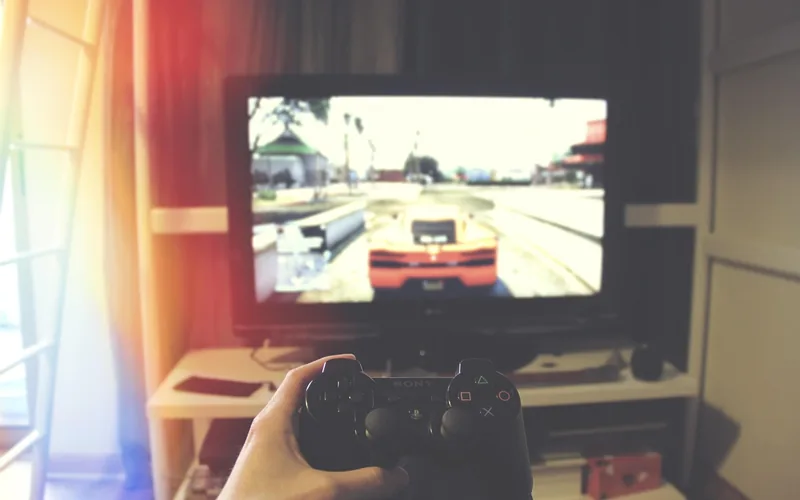 Open-world driving game on a TV screen with a controller held in the foreground