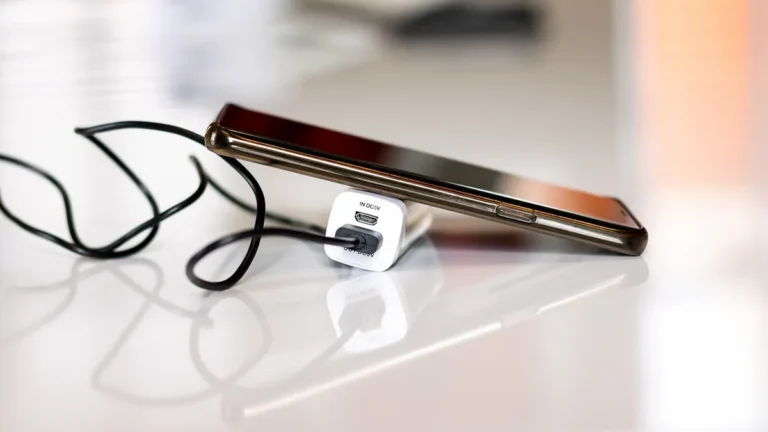 Smartphone lying on a white desk connected to a charger by a black cable