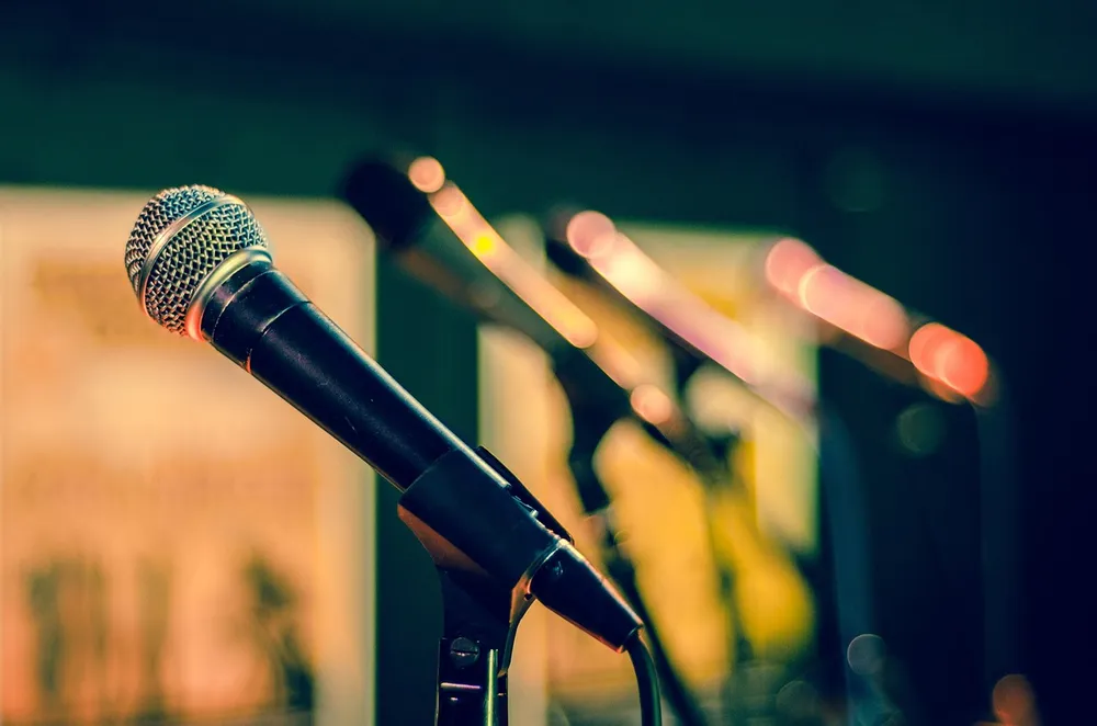 A black microphone on a stand in focus with blurred microphones and warm stage lights behind it