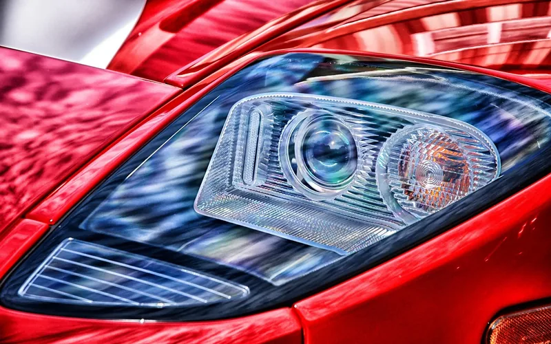 Glossy red painted body panels beside a headlight on a sports car