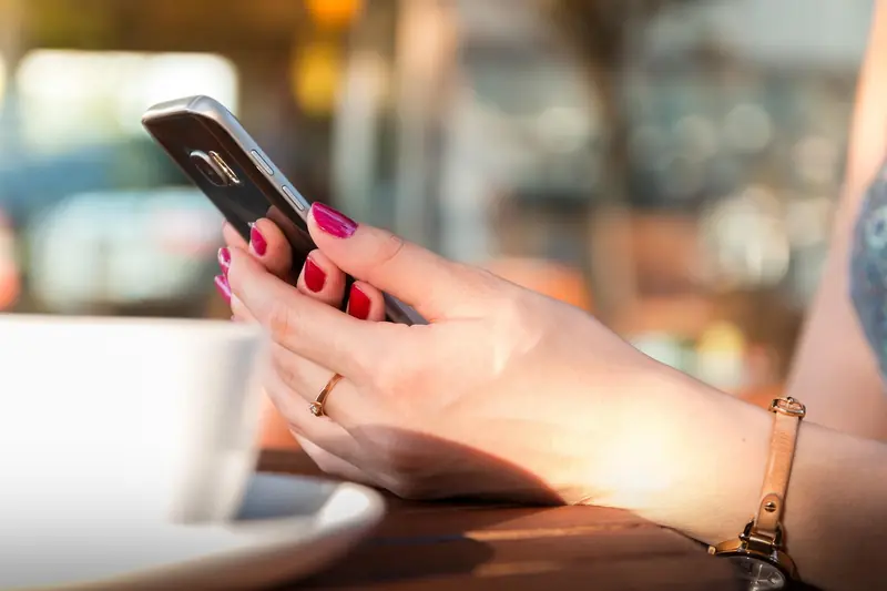 Hand holding a smartphone beside a white cup