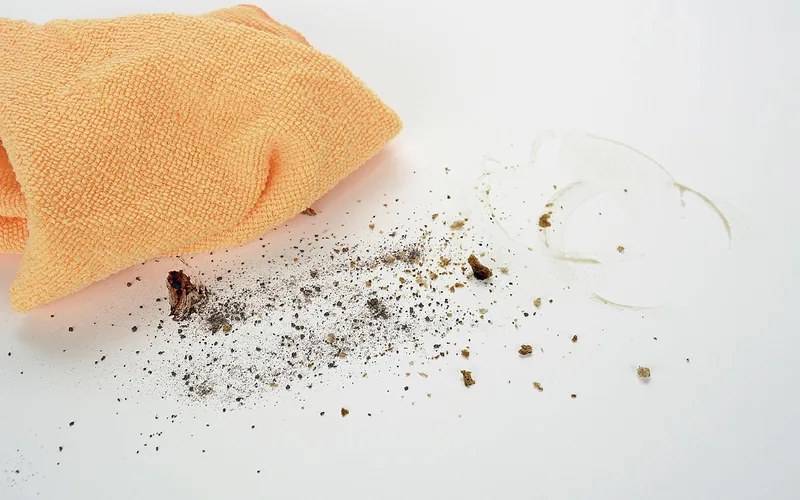 Orange microfiber cloth lying beside dust and crumbs on a white surface