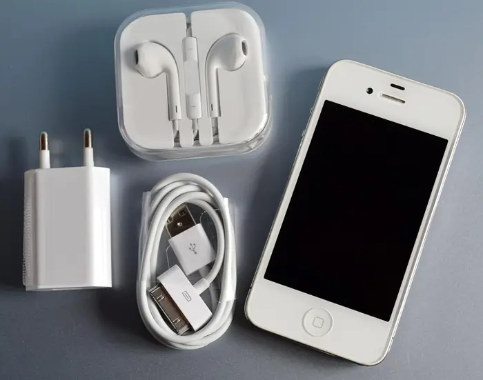 White smartphone beside earbuds, a charger and a USB cable on a gray surface