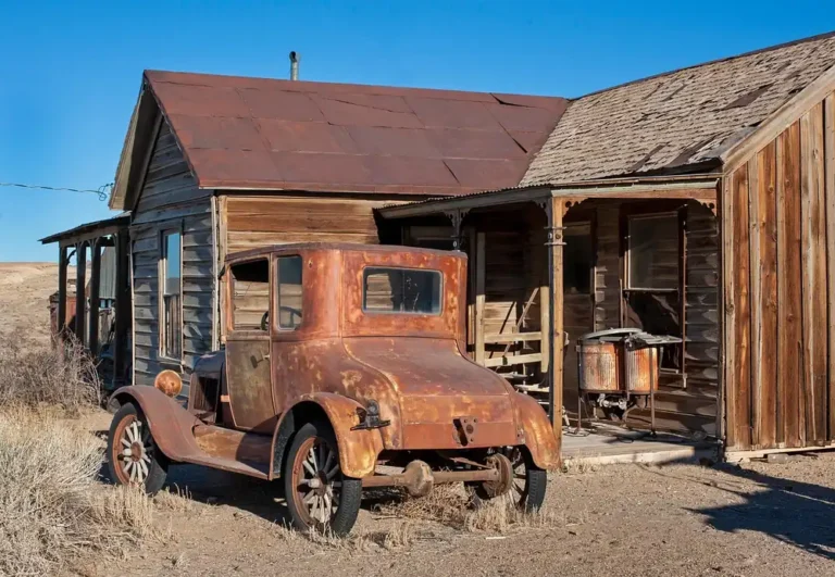 Weathered vintage car parked beside an old wooden building in the Nevada desert