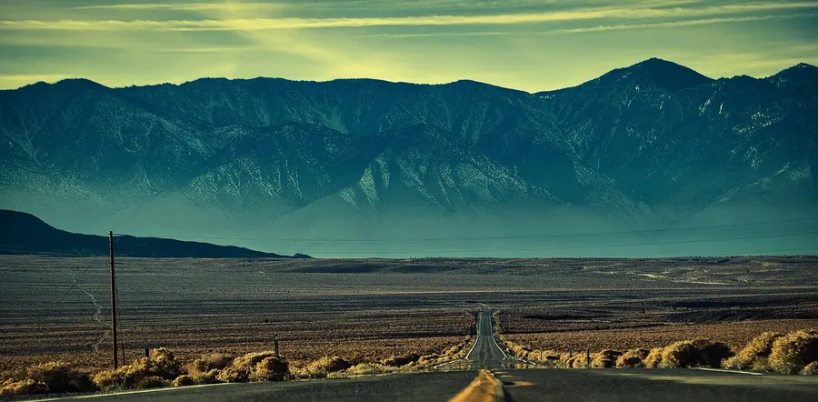 Straight desert road stretching toward a mountain range under a green evening sky