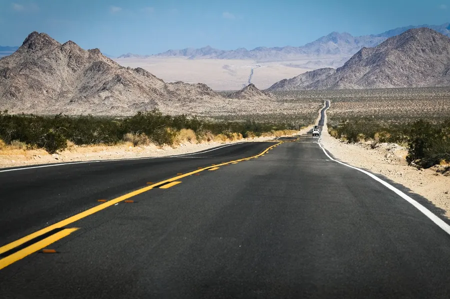 Two-lane desert highway running toward distant mountains in the American Southwest