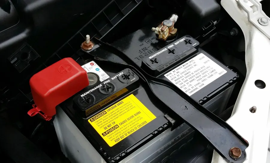 Car battery with a danger explosive gases warning label and red terminal cover
