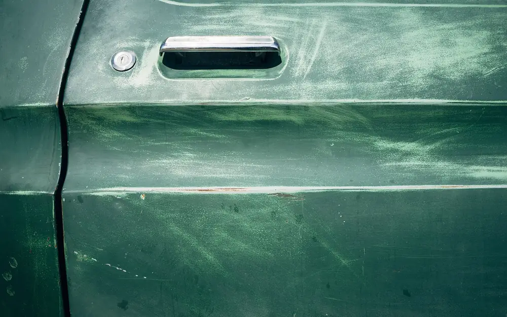Close-up of a green car door showing the handle, lock and the shut line between the door and the body