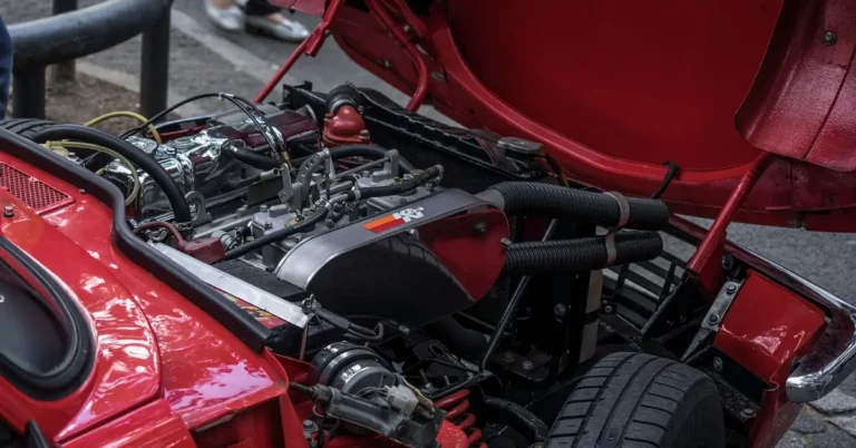 Red classic car with the hood held open by a support rod and the engine visible