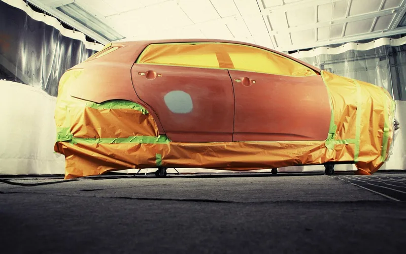 Car masked with paper and tape inside a paint booth during a repaint