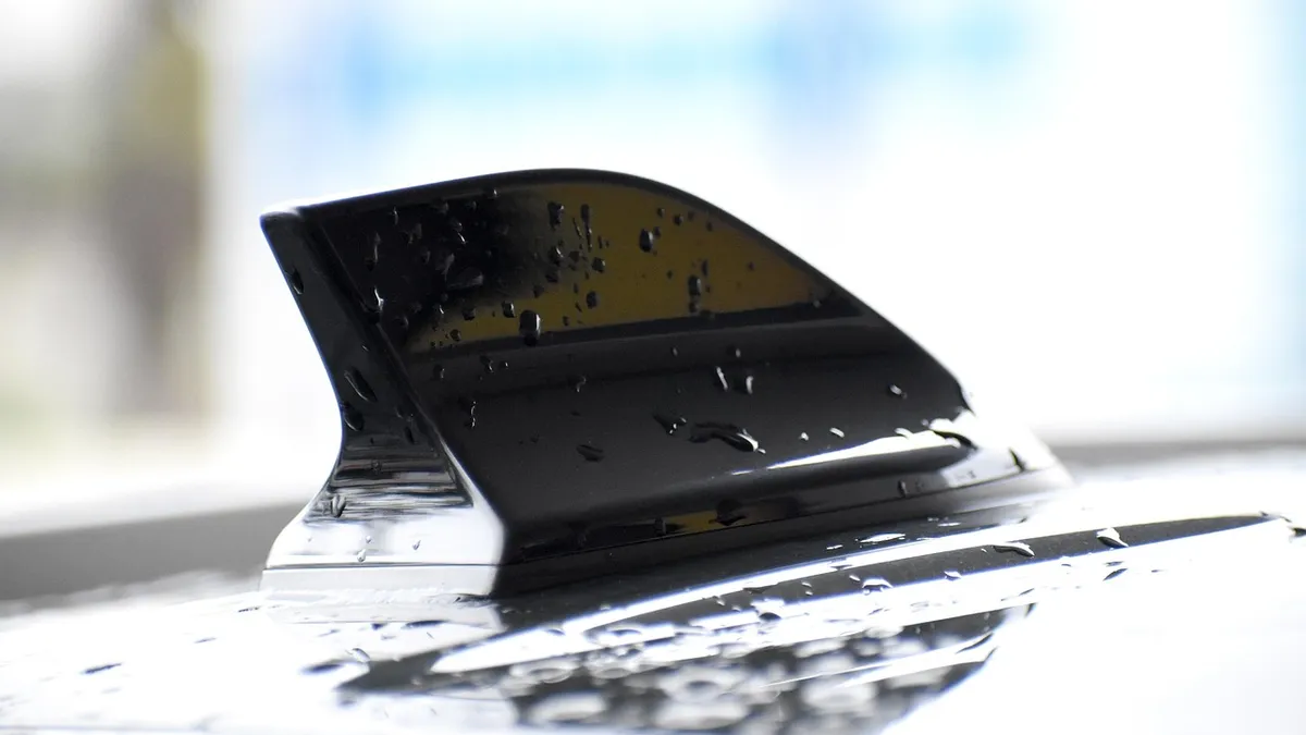 Black shark-fin style antenna mounted on a car roof, covered in raindrops