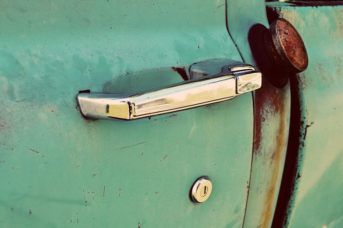 Chrome car door handle with a keyhole below it on an old green door