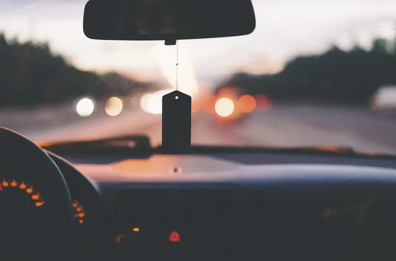 Flat tag-style air freshener hanging from a rearview mirror on a dusk drive