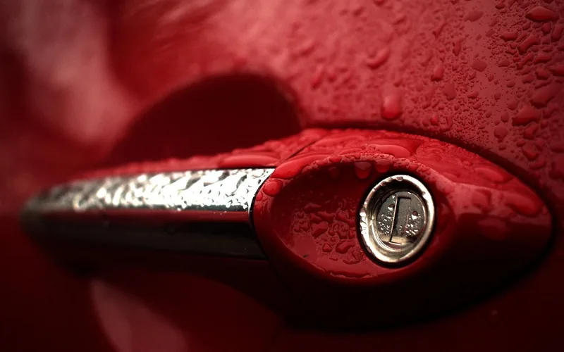 Car door handle with a key cylinder, covered in water drops