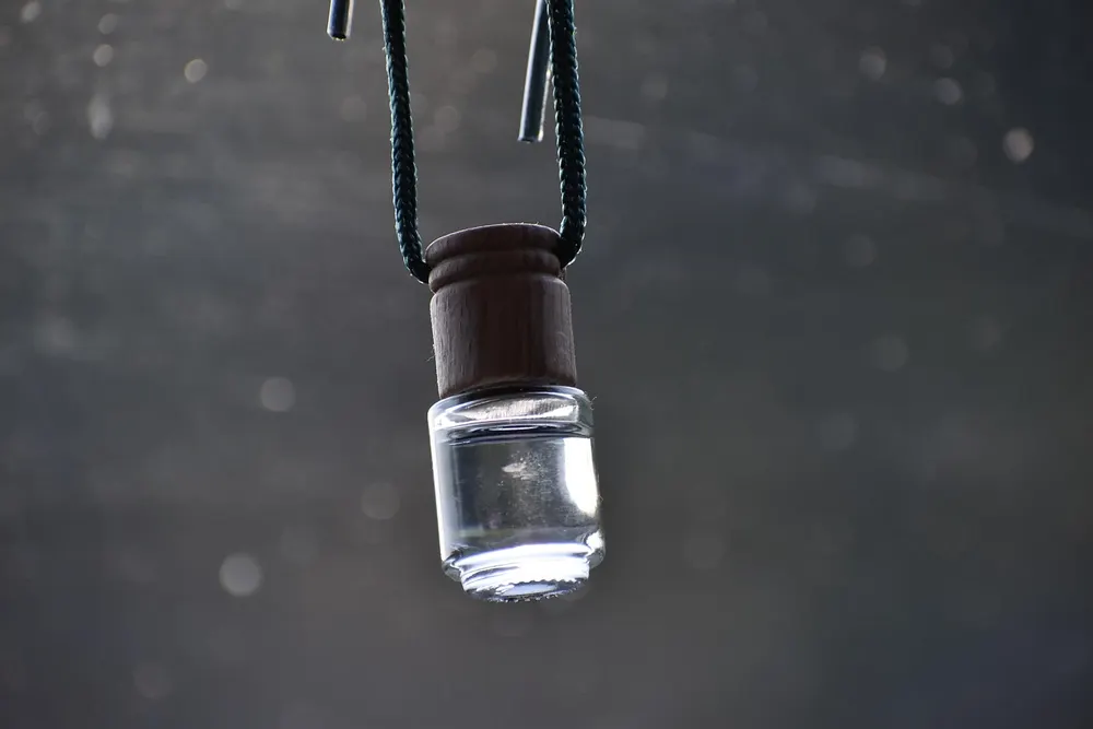 Small glass bottle air freshener with a wooden cap hanging from a cord