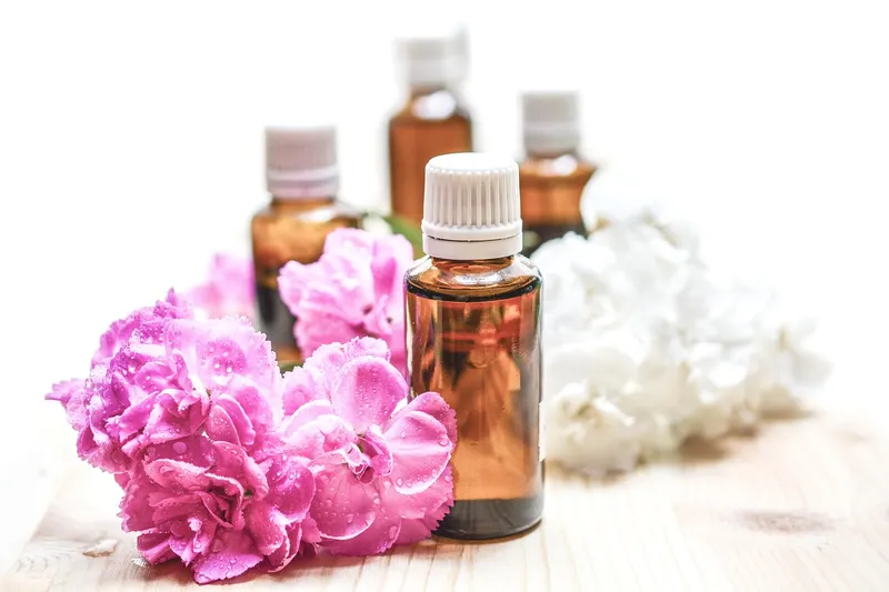 Small amber glass bottles of fragrance oil beside pink and white flowers