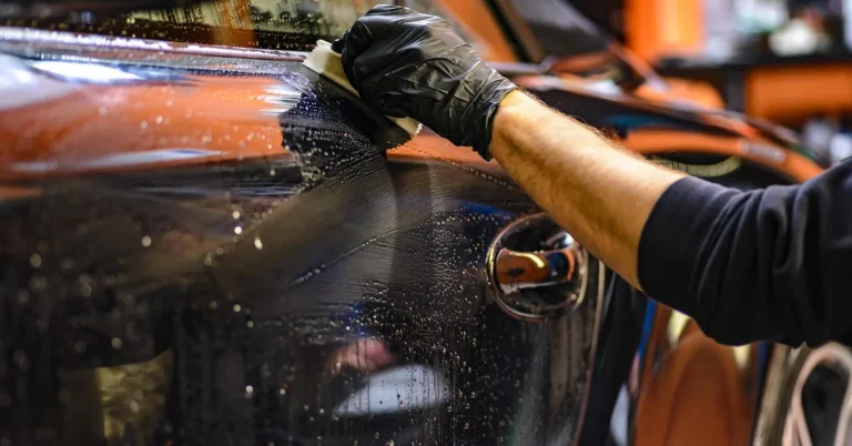 Gloved hand wiping wet paint on a car body during a detail
