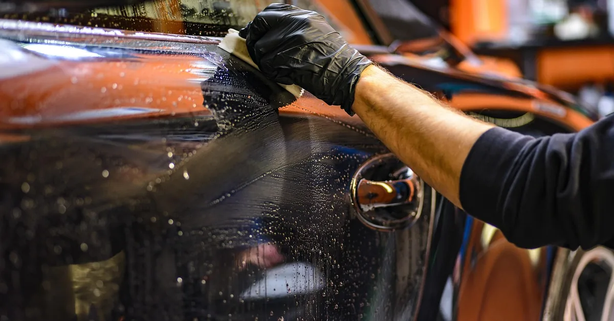 Gloved hand wiping wet paint on a car body during a detail