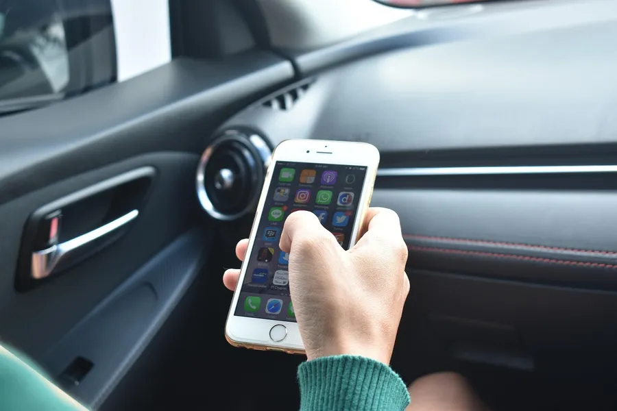 Hand holding a smartphone inside a car next to the dashboard air vent